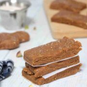 Three gingerbread protein bars stacked with parchment paper between them and pistachios around them.