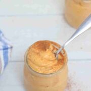Pumpkin protein pudding in a jar topped with cinnamon and a spoon in the jar.