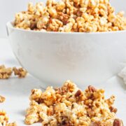 A white bowl filled with caramel popcorn and more popcorn in front of the bowl.