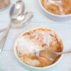 Pumpkin mug cake in a ramekin with coconut cream on top and a spoon in the cake.