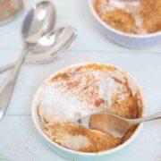 Pumpkin mug cake in a ramekin with coconut cream on top and a spoon in the cake.
