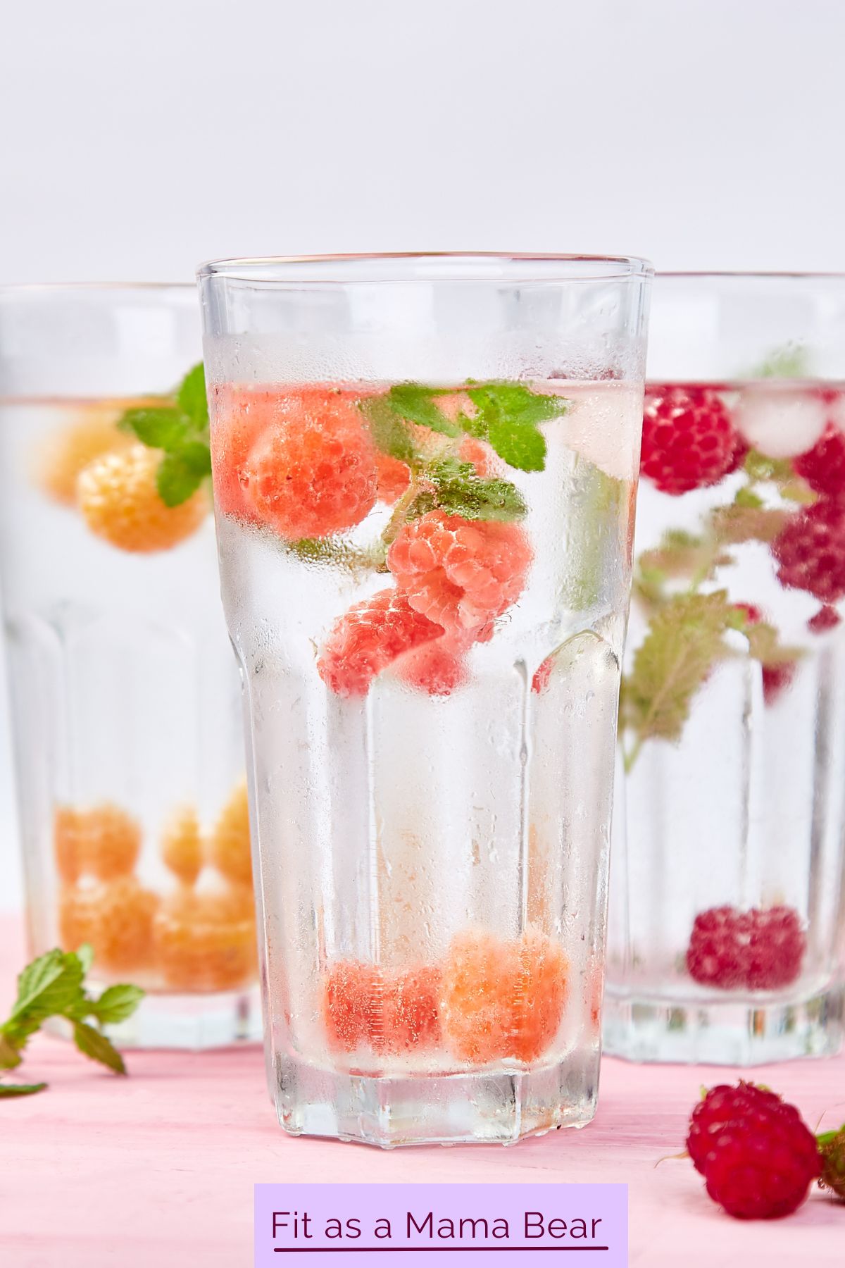 Three water glasses with berries and other fruit in them.