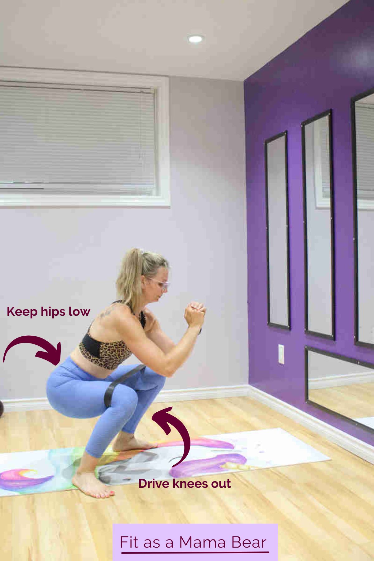 A woman in blue pants and sports bra performing a squat with a mini band.