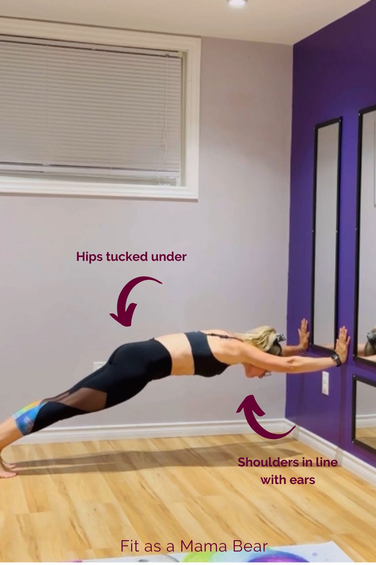 Woman in shorts and sports bra holding a hollow body hold on a wall.
