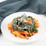 A plate of pasta with spinach, noodles, and parmesean on top and a blue linen behind it.