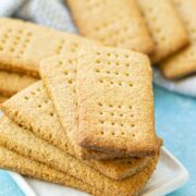 Gluten-free graham crackers stacked on a white plate with more graham crackers behind it.