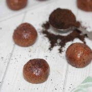 Coffee protein balls covered in cocoa powder with a spoon of coffee grinds beside them.