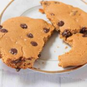 White plate with large single serving protein cookie broken in half with chocolate chips in it.