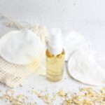 Small bottle with homemade face toner in it with cotton pads, calendula, and a linen around it.