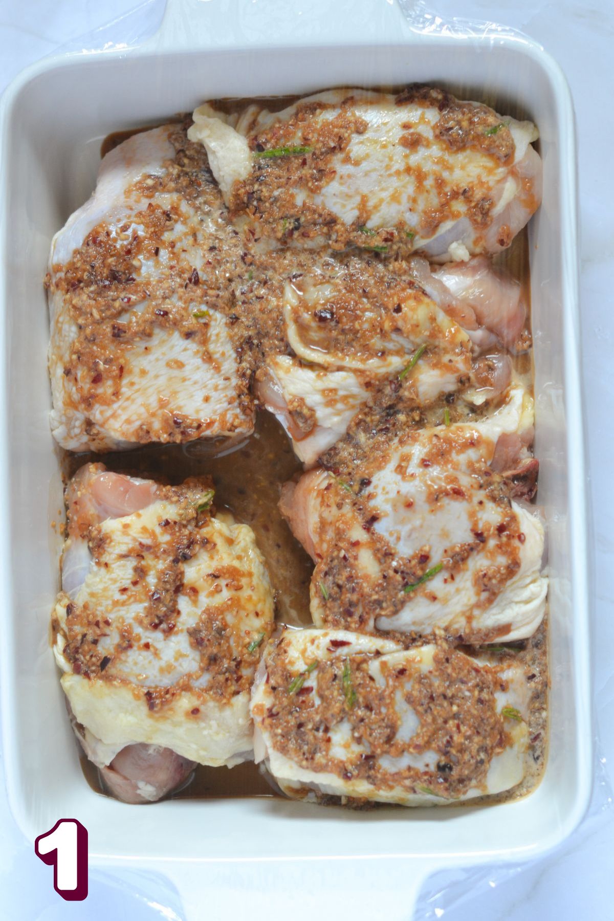 Marinade on top of chicken thighs in a white baking dish.