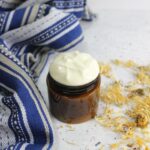 Whipped shaving lotion in an amber jar with a blue linen and calendula flowers around it.