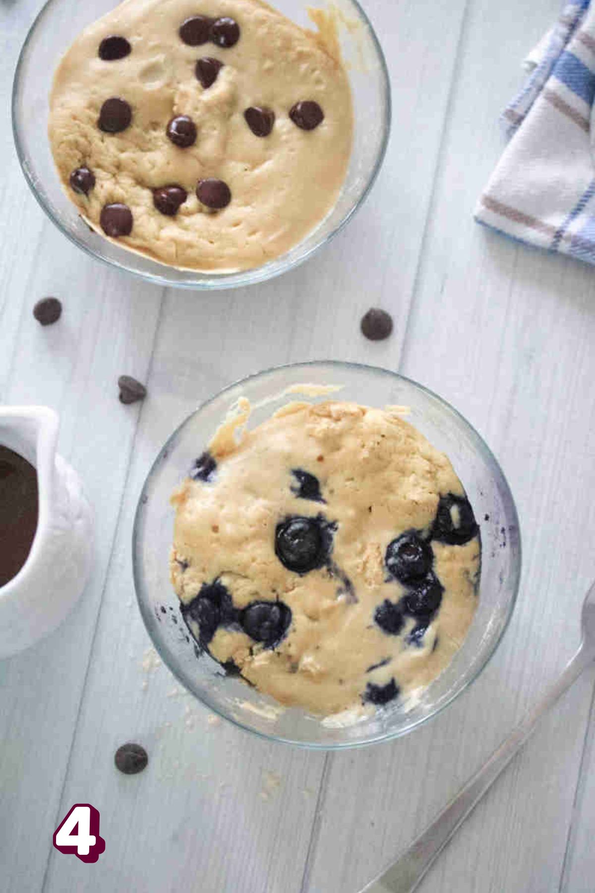 Two bowls with microwave protein pancakes in the one topped with chocolate chips and the other blueberires.