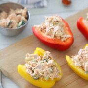 Red and yellow peppers sliced and stuffed with tuna salad on a wooden cutting board.