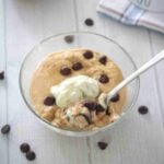 Glass bowl with a protein mug cake topped with chocolate chips and a dollop of whipped cream and a spoon in the bowl.
