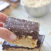 Two fingers placing a chocolate topped protein rice krispie treat on top of another one.