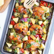a sheet pan of baked chicken thighs with pineapples, broccoli, peppers, and onions with a wooden spoon at the top portion