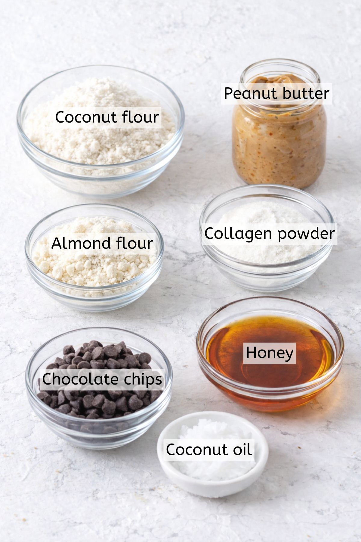 Coconut flour, peanut butter, sweetener, chocolate chips, and walnuts in bowls with text labels over top.
