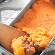 Wooden spoon pulling out some sweet potato shepherds pie from a baking dish.