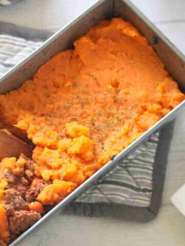Wooden spoon pulling out some sweet potato shepherds pie from a baking dish.