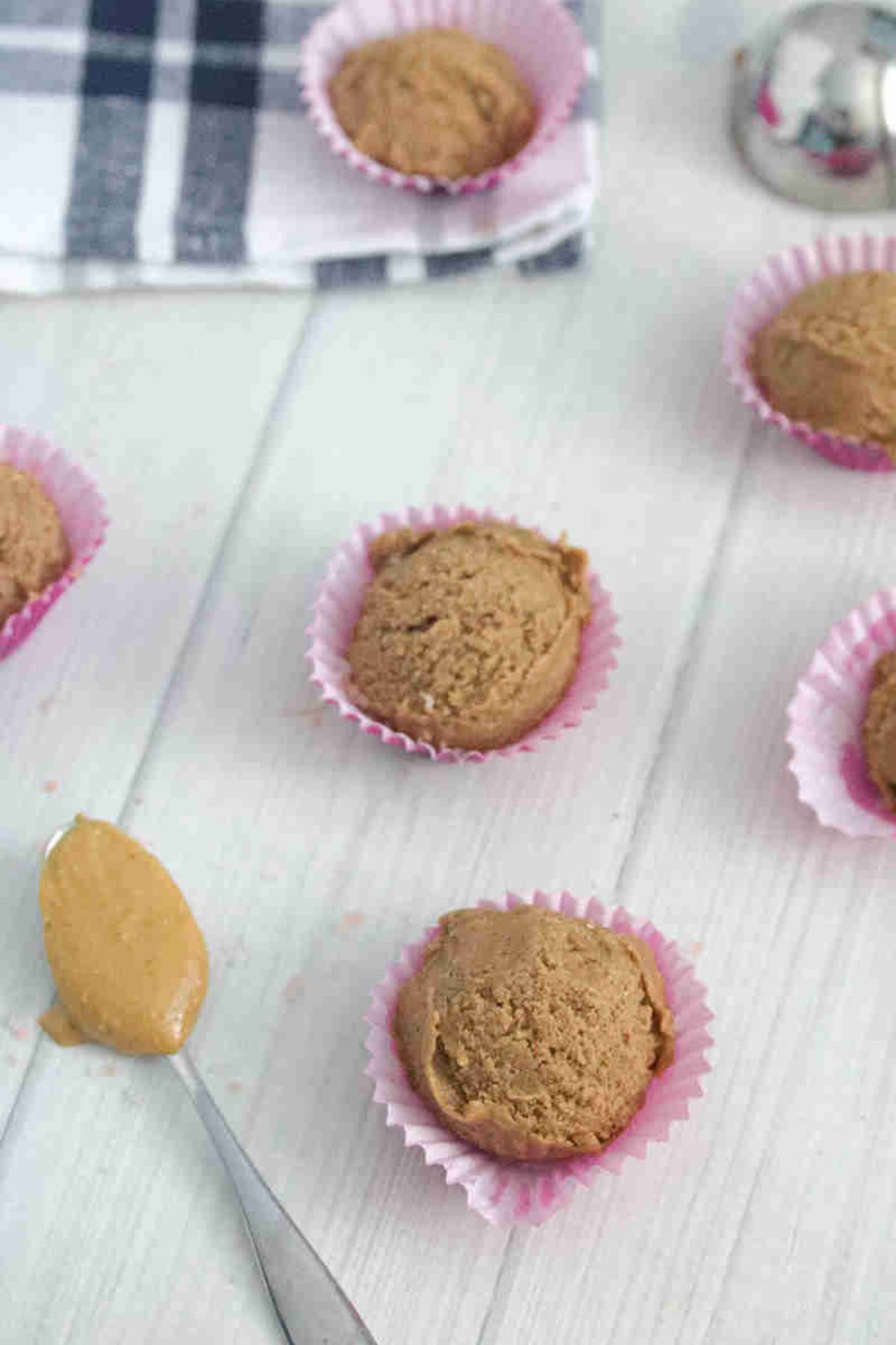 Chocolate peanut butter protein balls on mini cupcake liners with a spoonful of peanut butter at the bottom left.