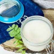 Glass jar with DIY leave in conditioner in it on a wooden board with a linen behind it.