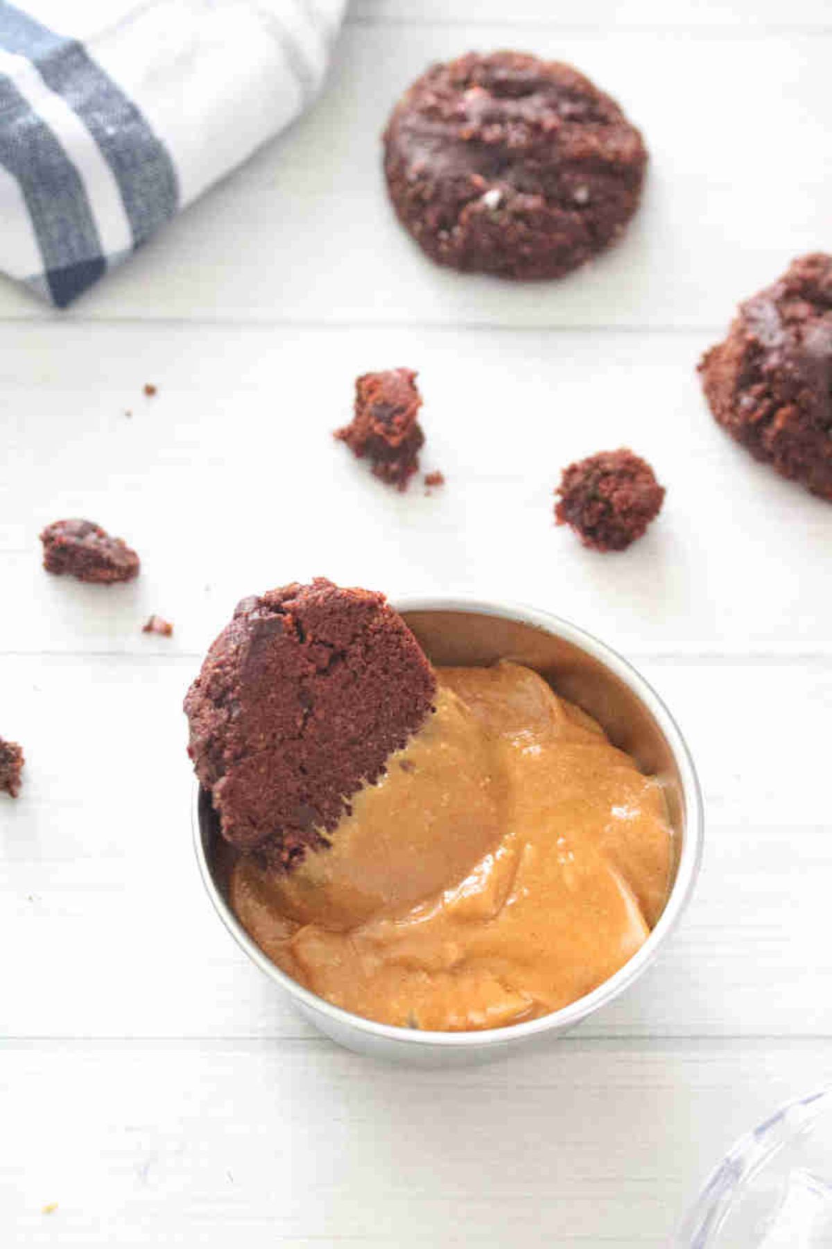 Chocolate cookie dunked into a bowl of protein cookie butter with more cookies behind it.