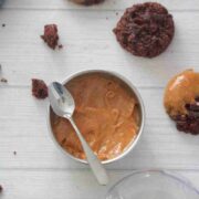 Protein cookie butter in a steel bowl with a spoon on it and chocolate cookies around it.