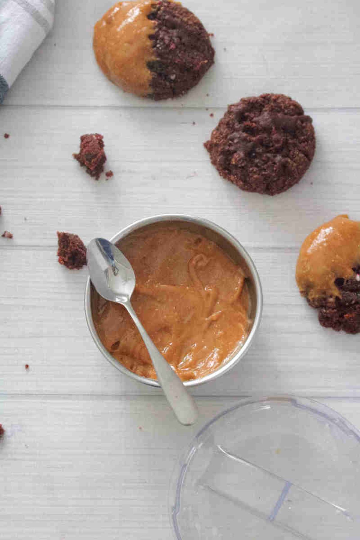 Protein cookie butter in a steel bowl with a spoon on it and chocolate cookies around it.