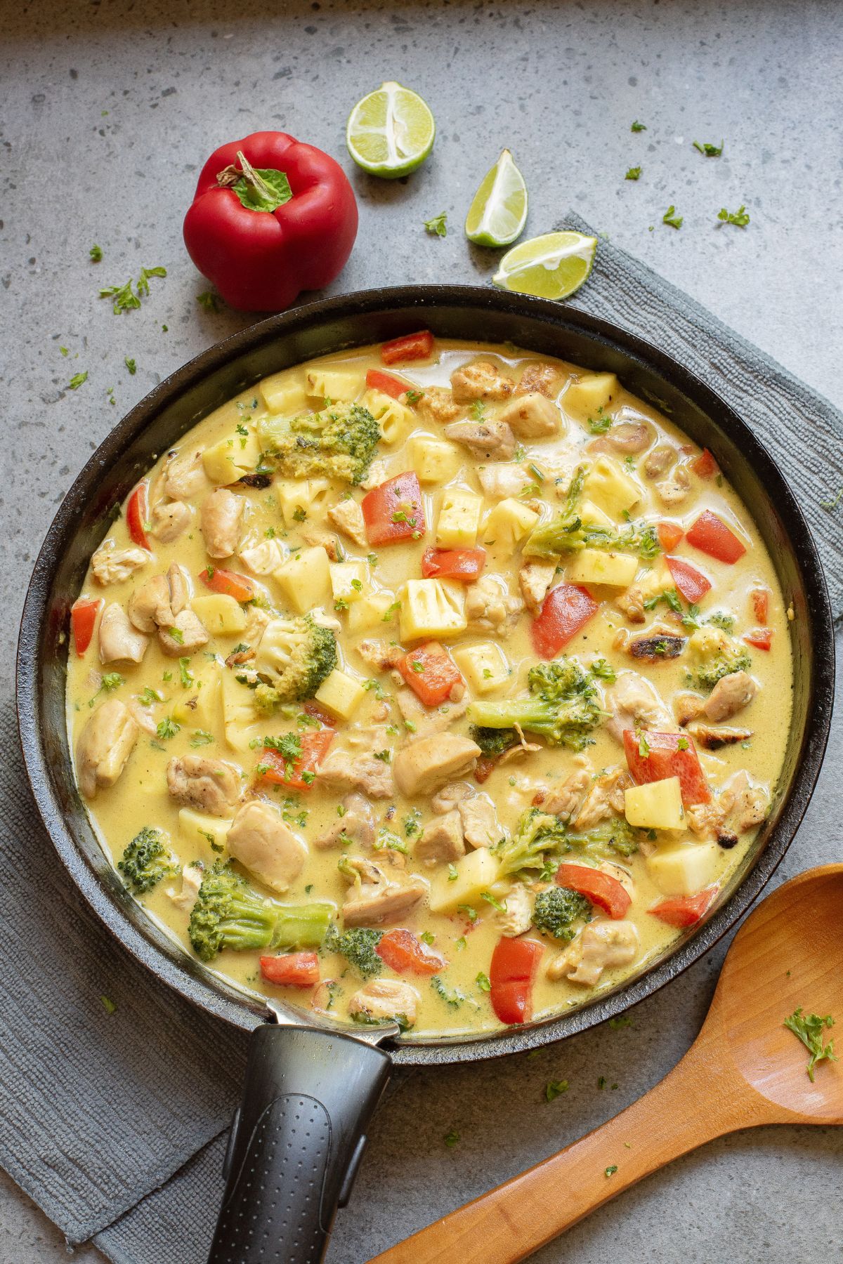 Green chicken curry with pineapple and peppers in a skillet with a wooden spoon beside it.