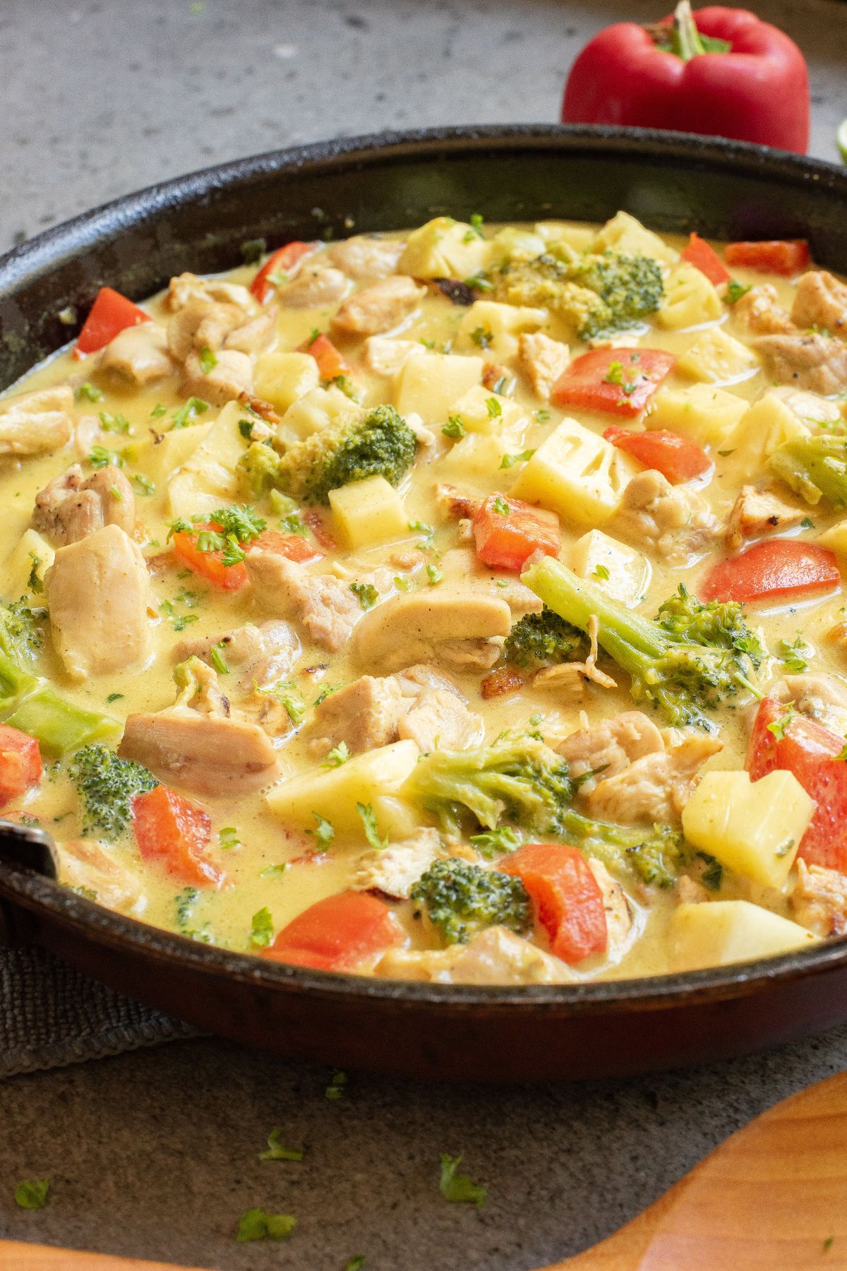 Green chicken curry with pineapple and peppers in a skillet with a wooden spoon.