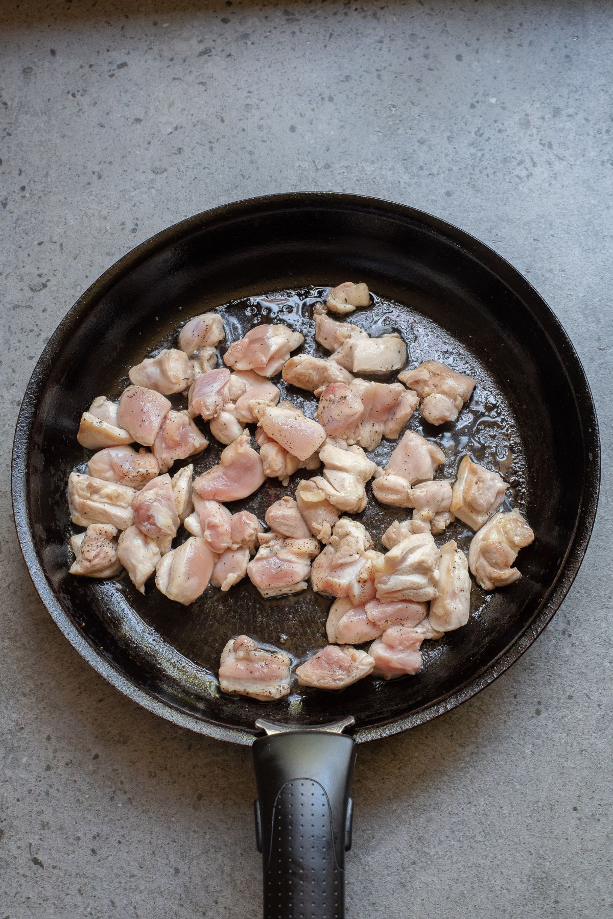 Raw chicken seasoned with salt and pepper in a black skillet.