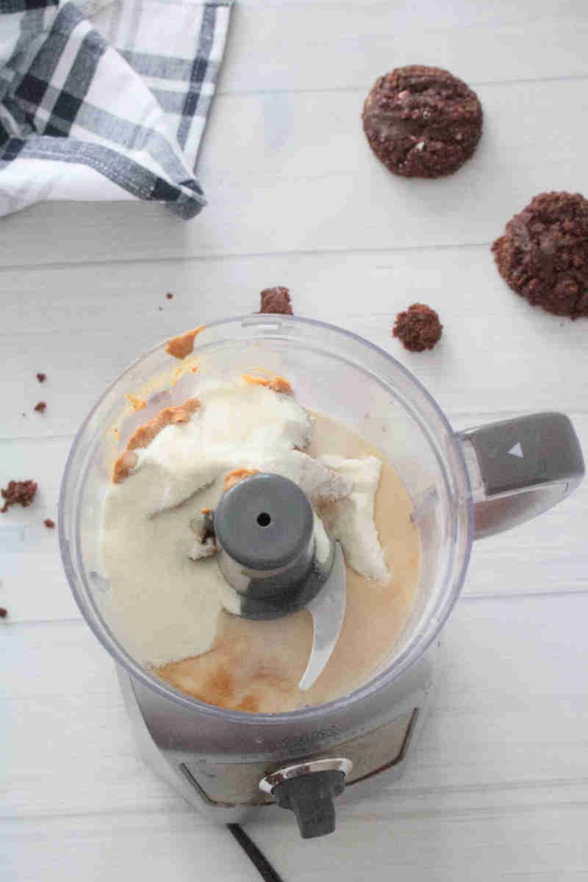 Mini food processor with peanut butter, milk, and collagen in it and cookies around it.