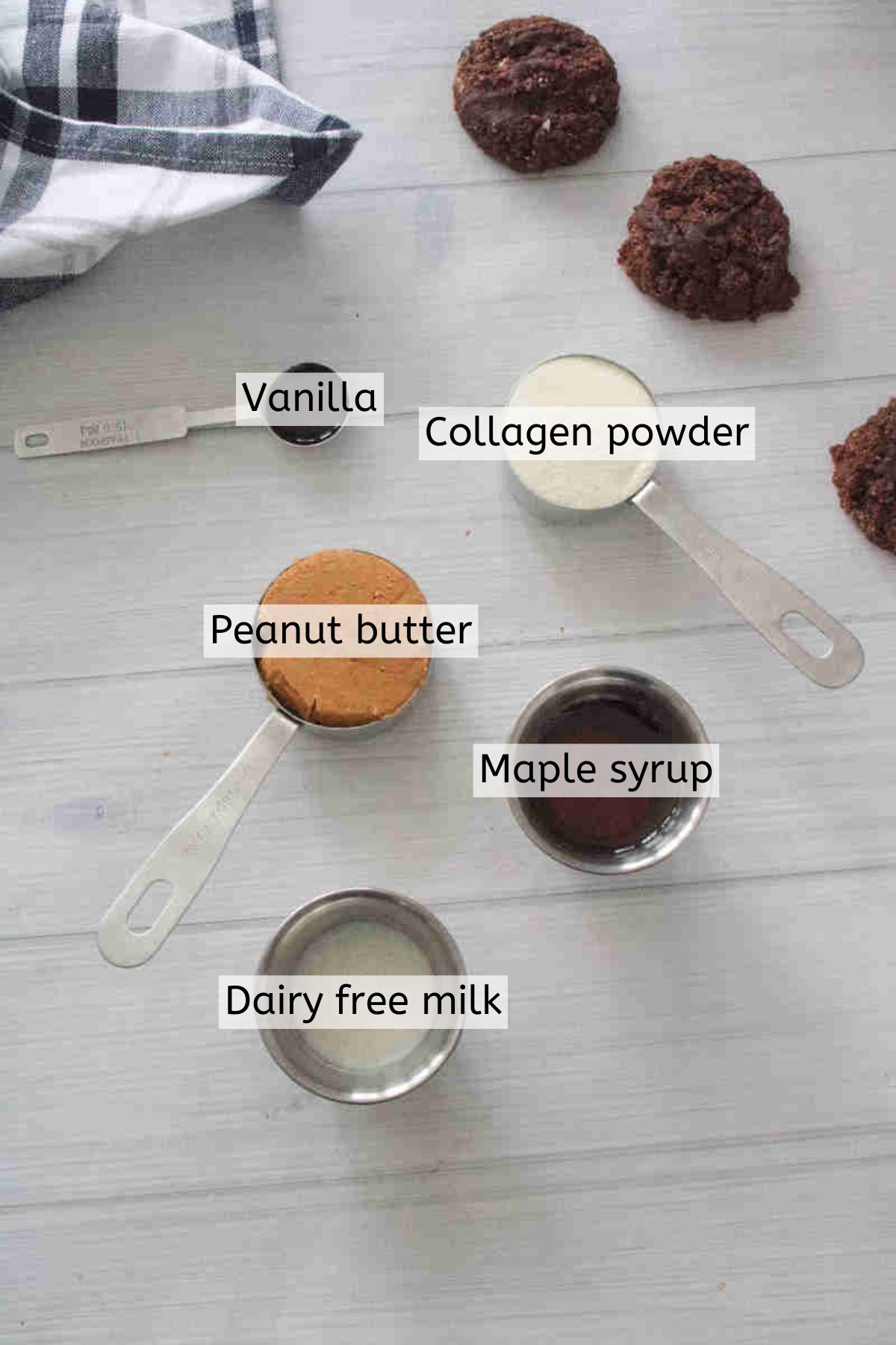 Ingredients to make homemade cookie butter like milk, peanut butter, maple syrup, and collagen in measuring cups with text labels over top.
