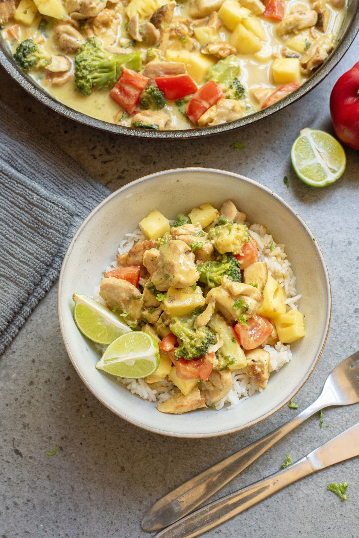 Green chicken curry with pineapple in a bowl with vegetables and a skillet with more curry behind it.