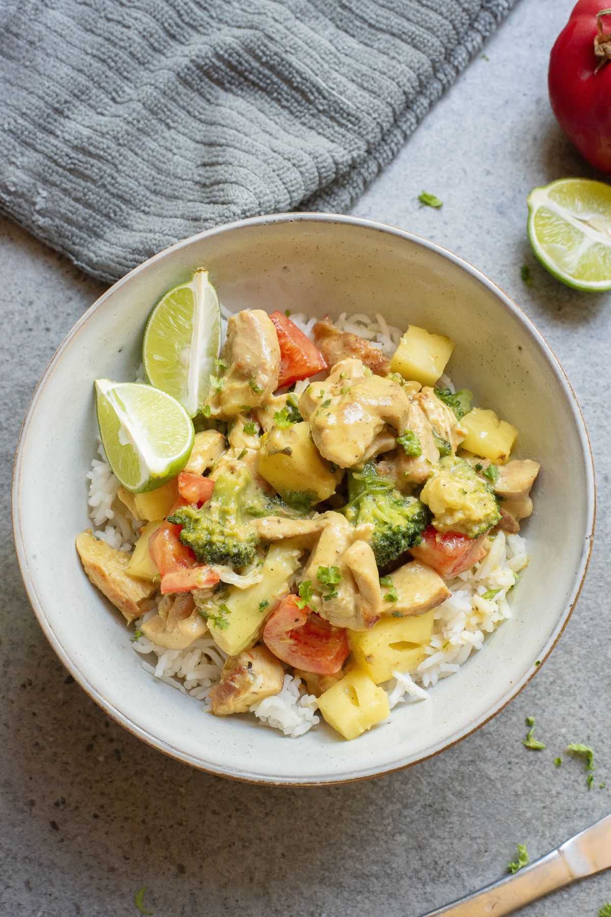 Green chicken curry with pineapple in a bowl with vegetables and a linen around it.