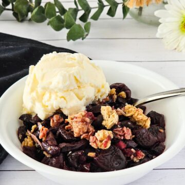 Cherry granola crisps in a bowl with a scoop of ice cream and a metal spoon.