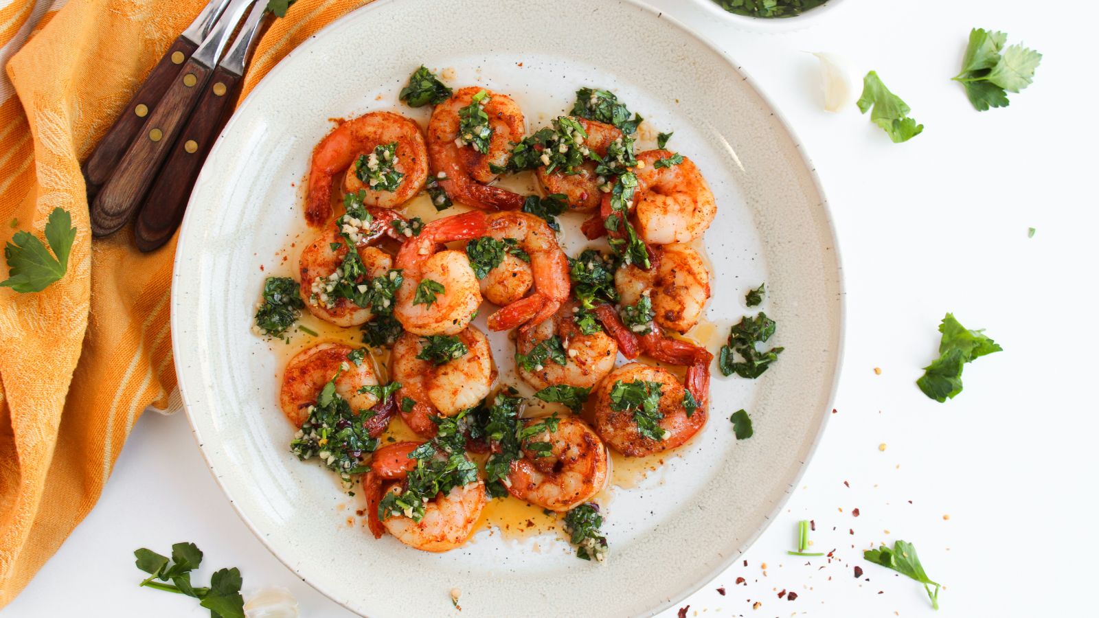 A plate of chimichurri shrimp with a set of forks on a kitchen towel at the side.