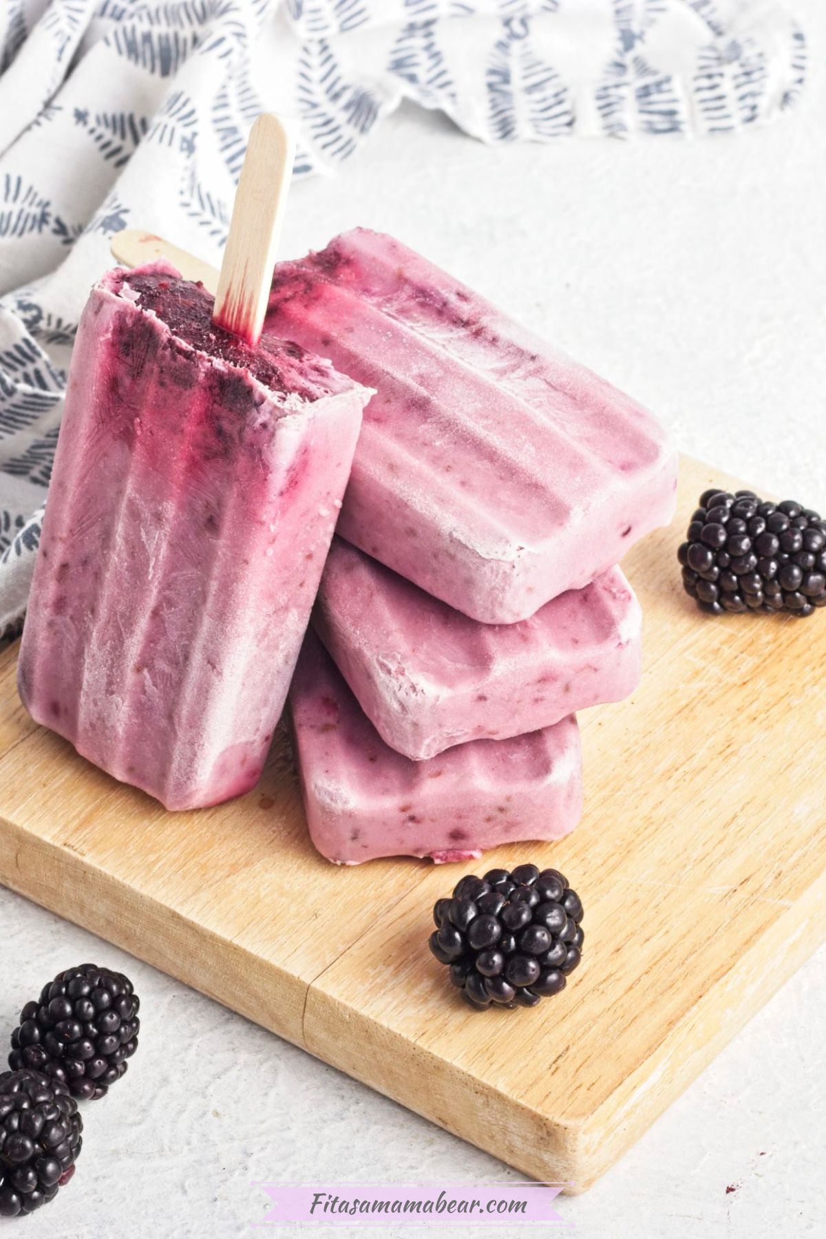 black berry popsicles stacked on top of each other on a wooden board with blackberries around
