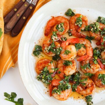 A plate of chimichurri shrimp with a set of forks on a kitchen towel at the side.