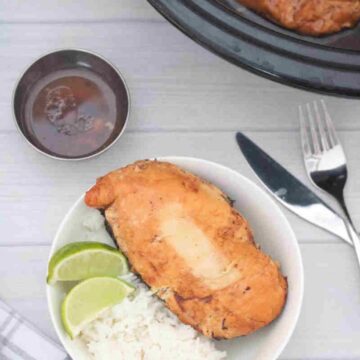 Large chicken breast in a white bowl with rice and lime with a slow cooker behind it.