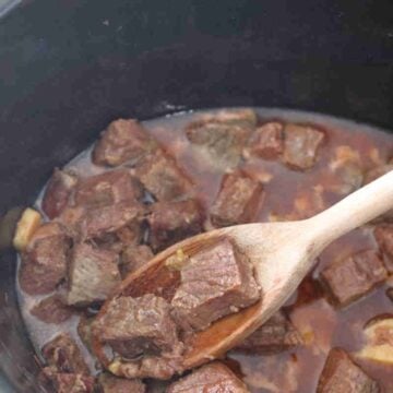 Slow cooked steak bites inside a pot with a wooden spoon.