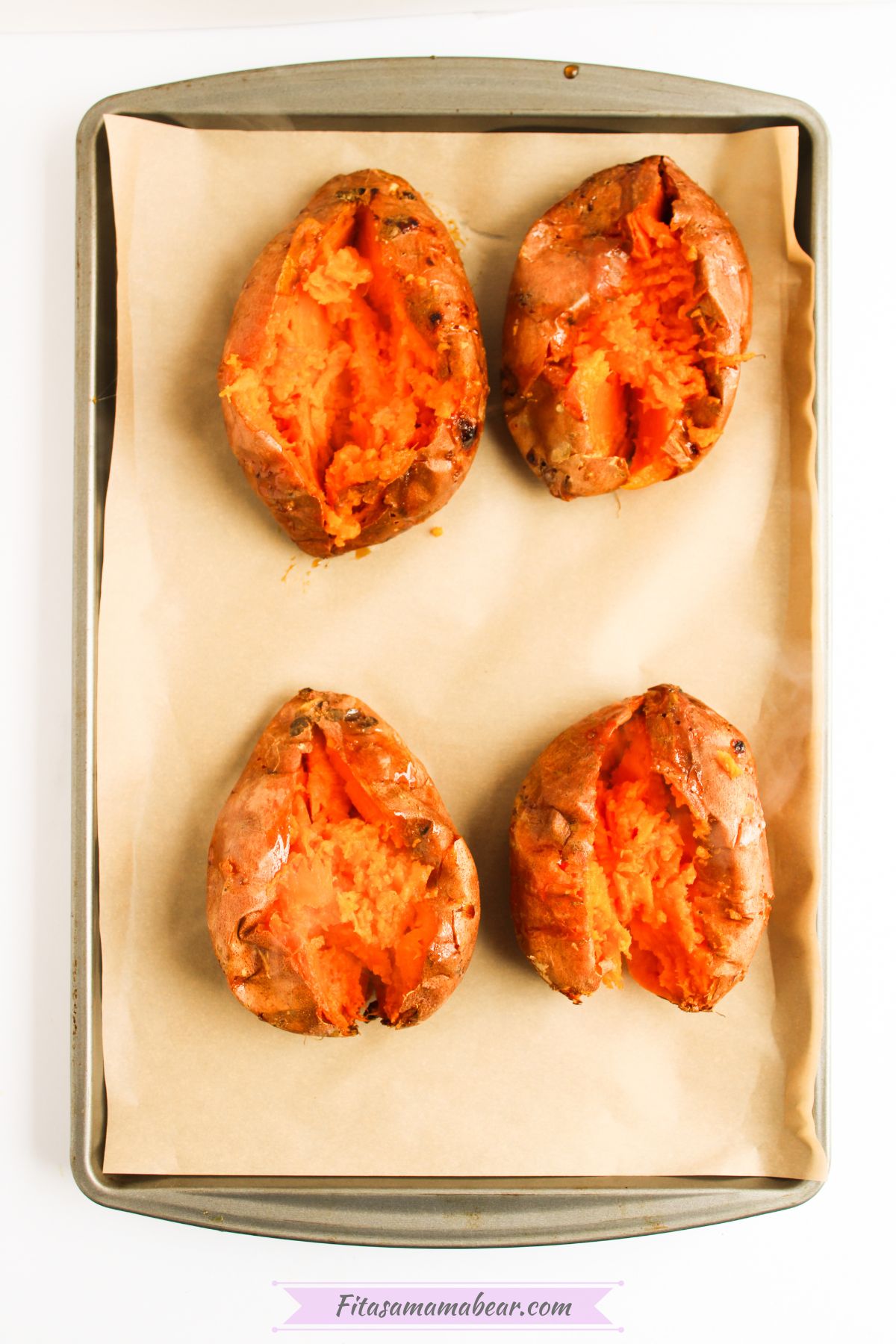 Baked sweet potatoes on a baking sheet sliced lengthwise and mashed with a fork.
