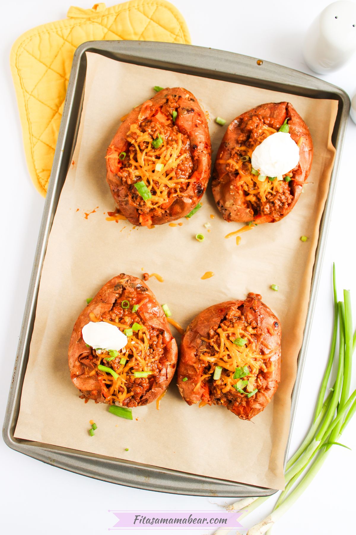 Baked sloppy joe sweet potatoes topped with sour cream and green onions on a baking sheet.