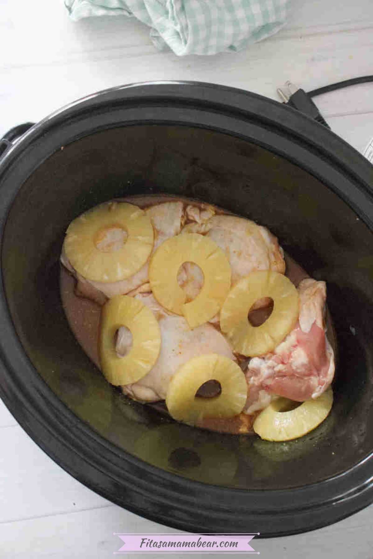 Tossed chicken in sauce topped with pineapple rings inside a slow cooker.