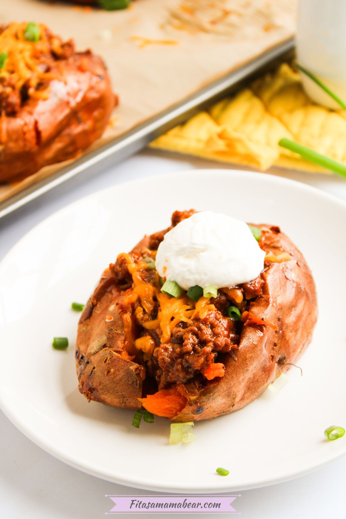 A plate of baked Sloppy Joe sweet potato with sour cream and green onions.
