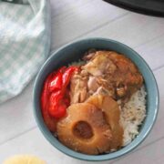 Slow cooker hawaiian chicken with pineapples and bell peppers on top of a bowl of rice.