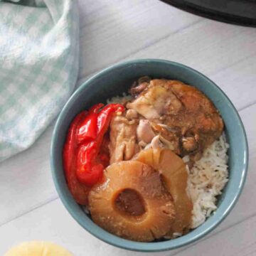 Slow cooker hawaiian chicken with pineapples and bell peppers on top of a bowl of rice.