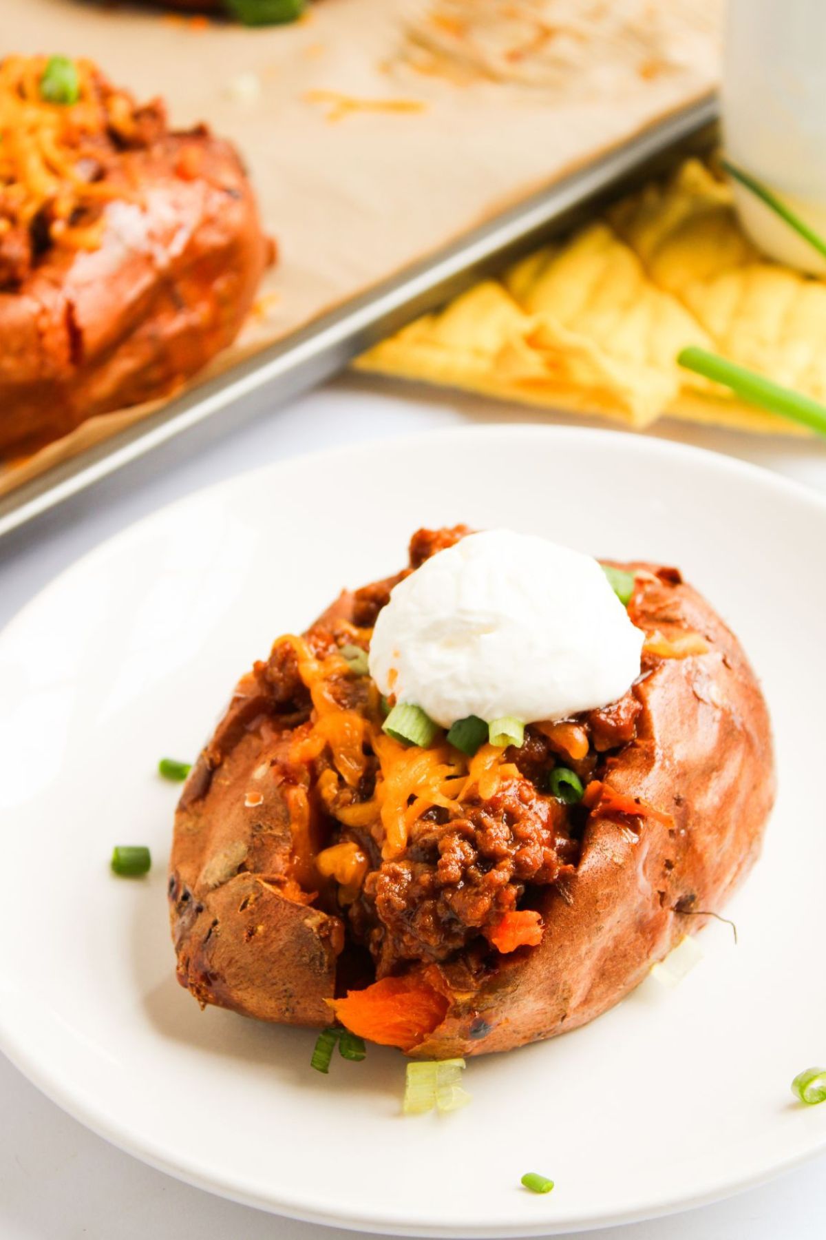 A plate of baked Sloppy Joe sweet potato with sour cream and green onions.