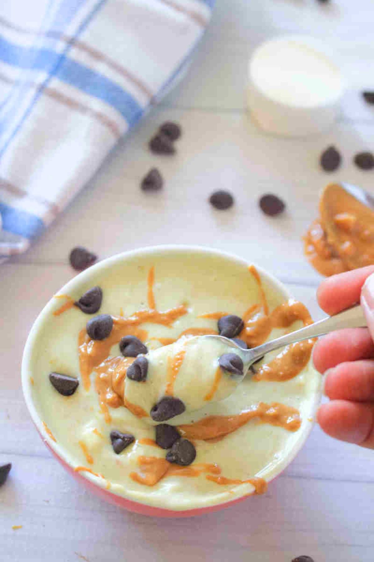 A bowl of greek yogurt protein pudding with chocolate chips and peanut butter swirl with a spoon scooping it.
