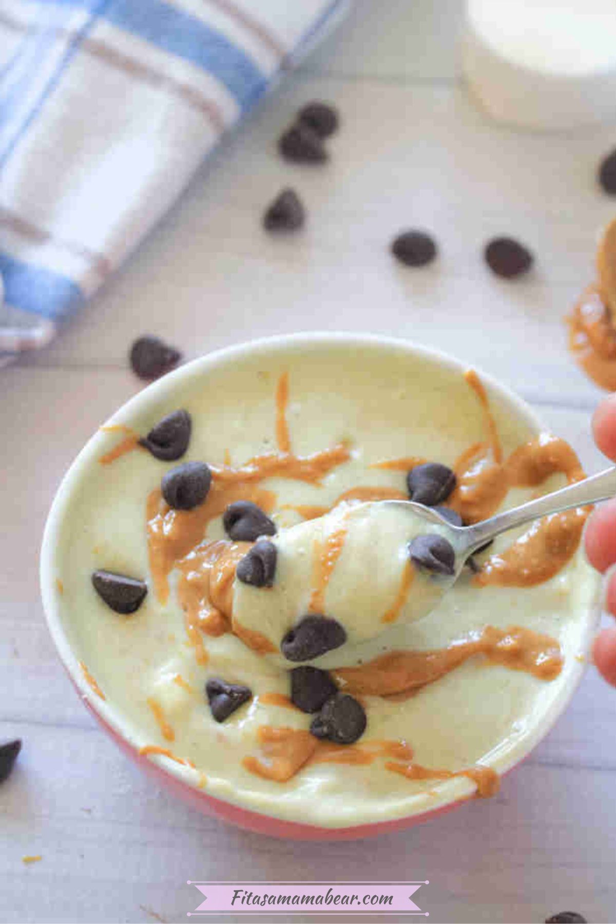 A bowl of greek yogurt protein pudding with chocolate chips and peanut butter swirl with a spoon scooping it.